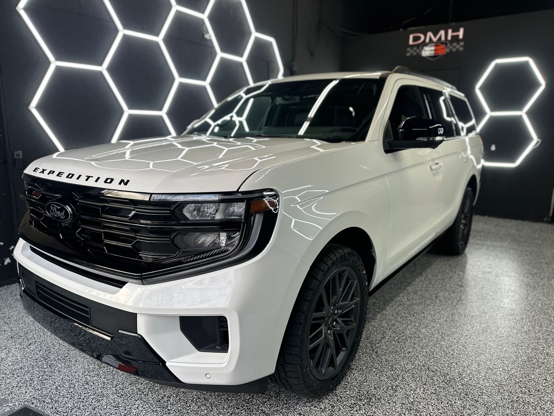White SUV in a showroom with black hexagon light wall and glossy floor.