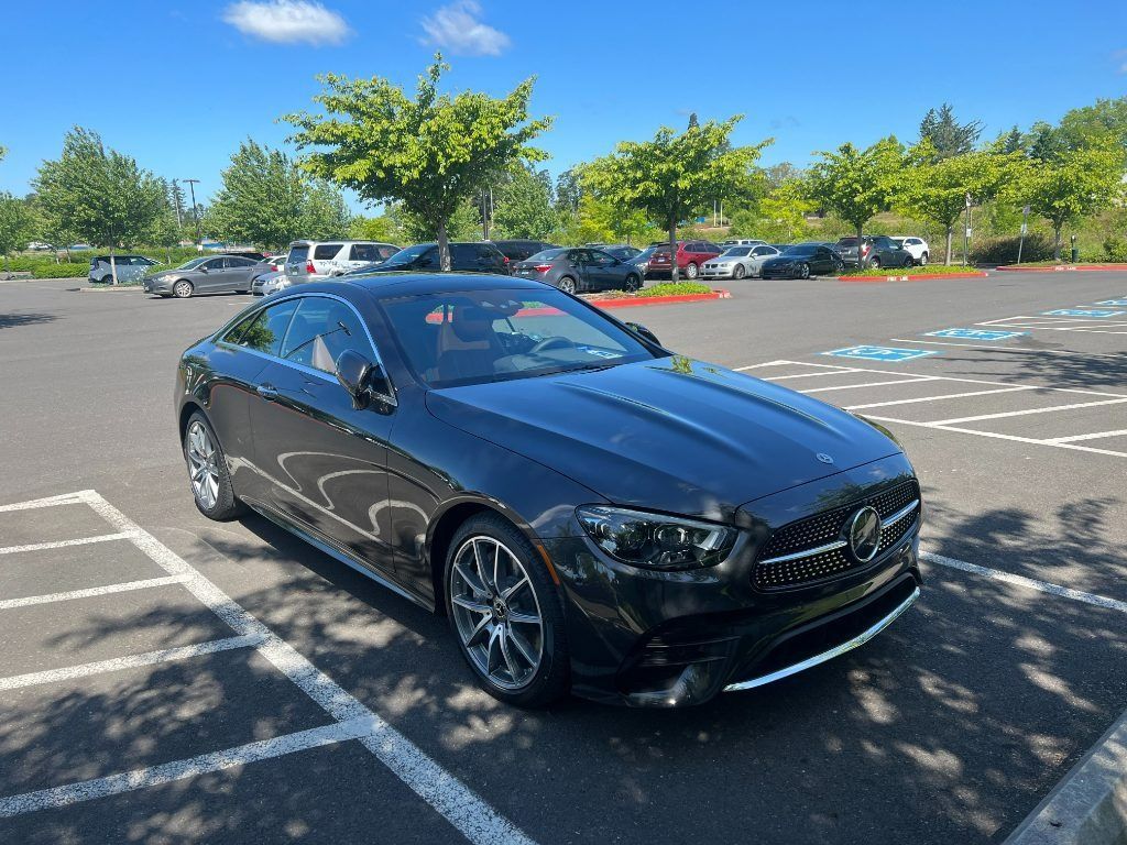 Black Mercedes coupe parked in a sunny lot with trees and other cars in the background