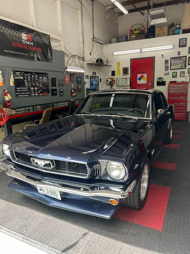 Dark blue classic Ford Mustang in a garage, front view with red-and-black floor tiles.
