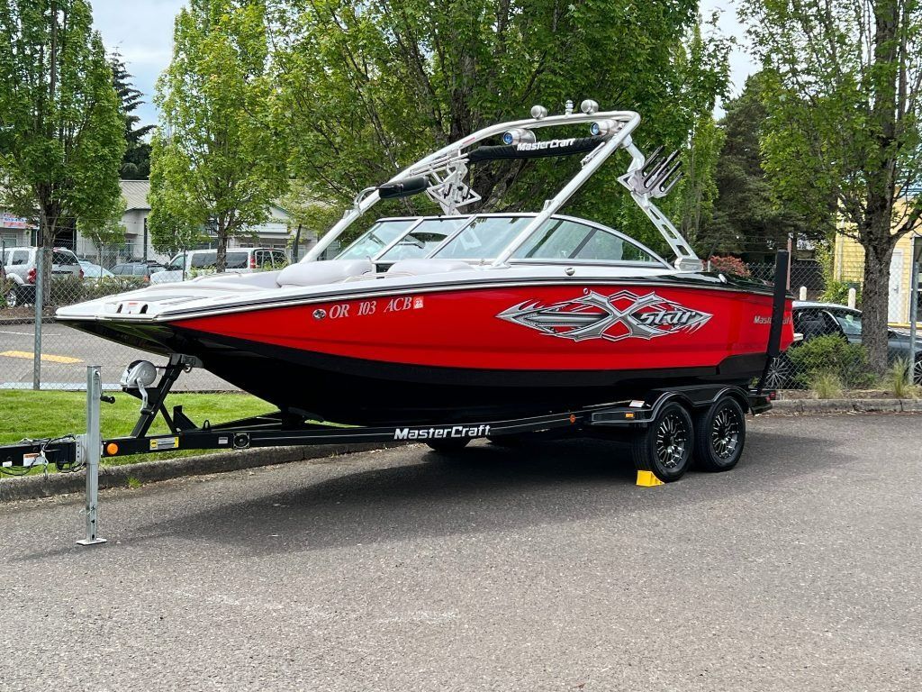 Red and black speedboat on a trailer in a parking lot, with trees in the background.