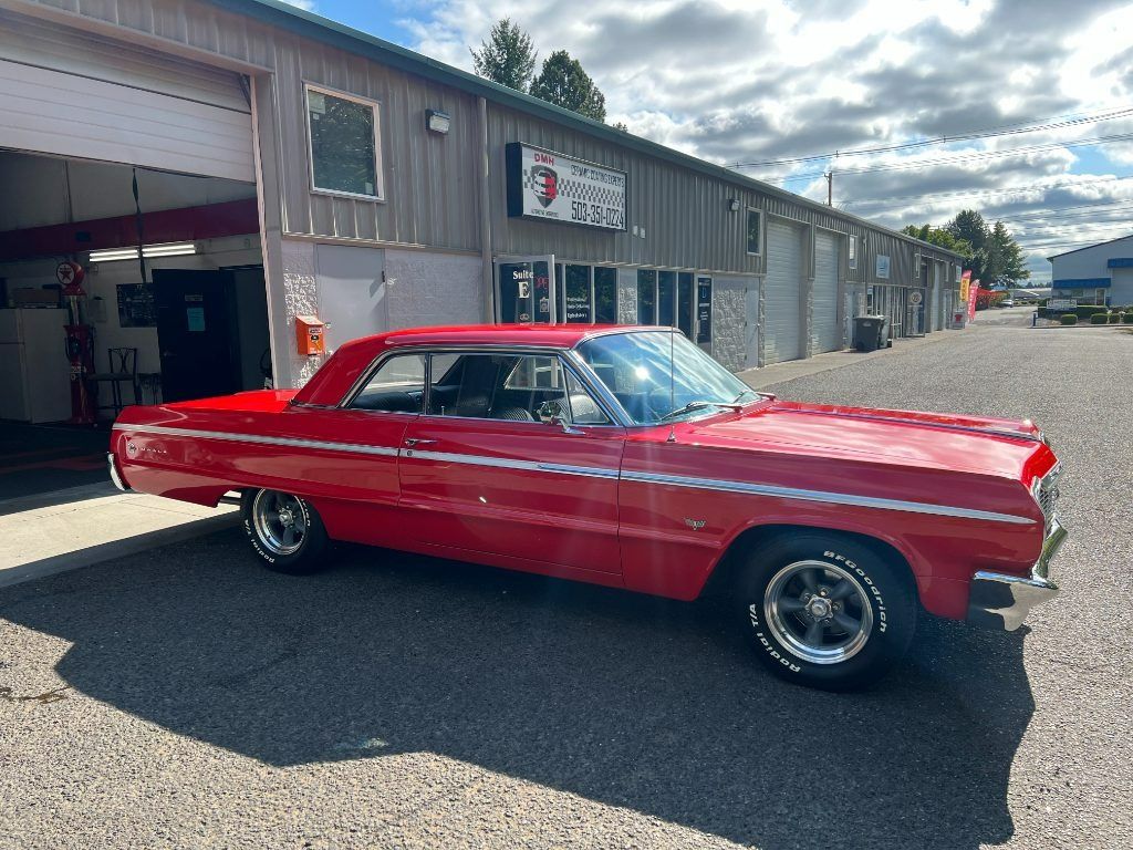Red classic car parked outside a garage under a cloudy sky