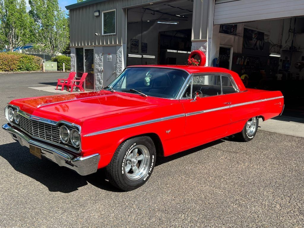 Bright red classic car parked outside a garage, front view in sunlight