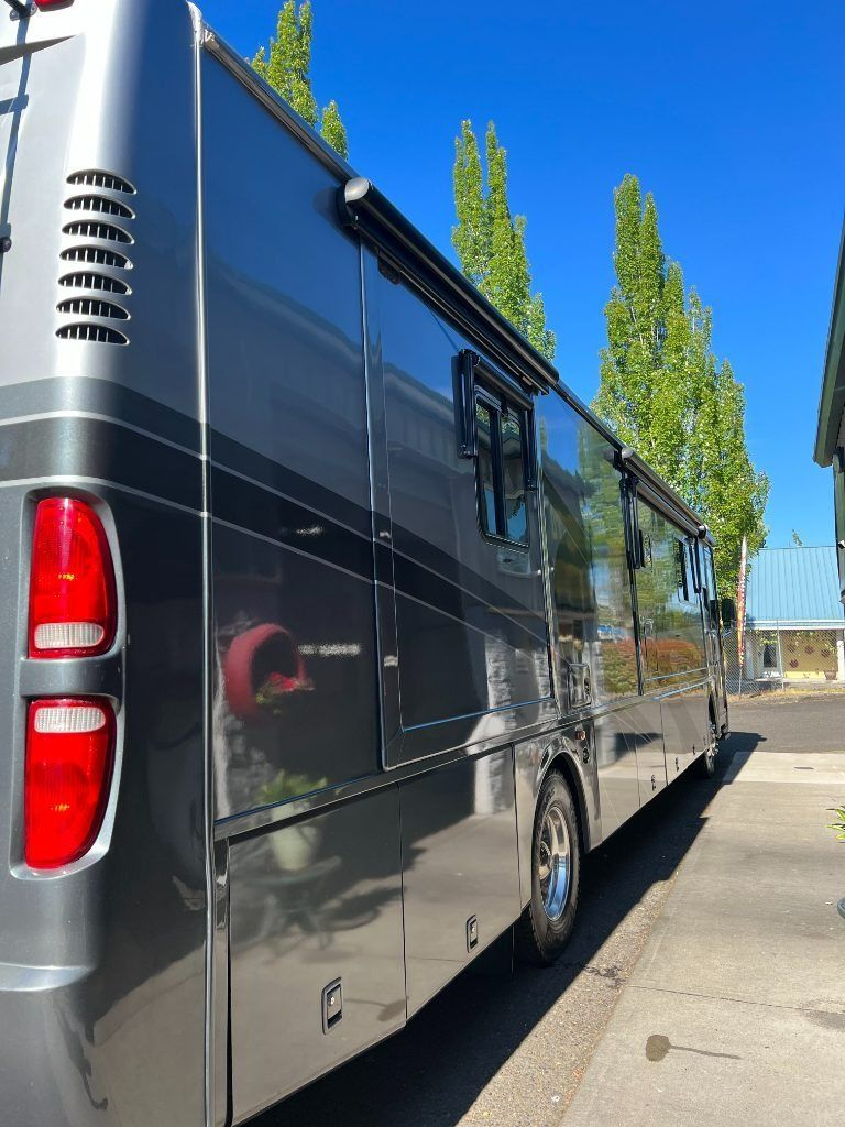 Black luxury van parked along a sunny fence-lined street under tall green trees