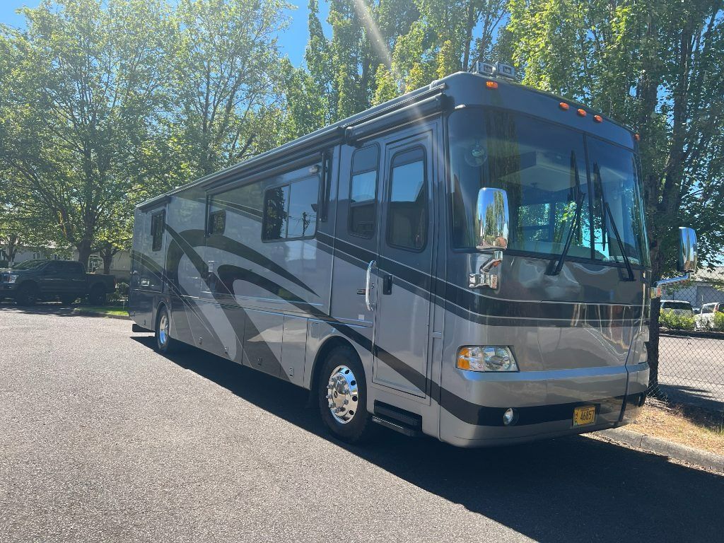 Silver and black RV parked on a sunny street lined with trees