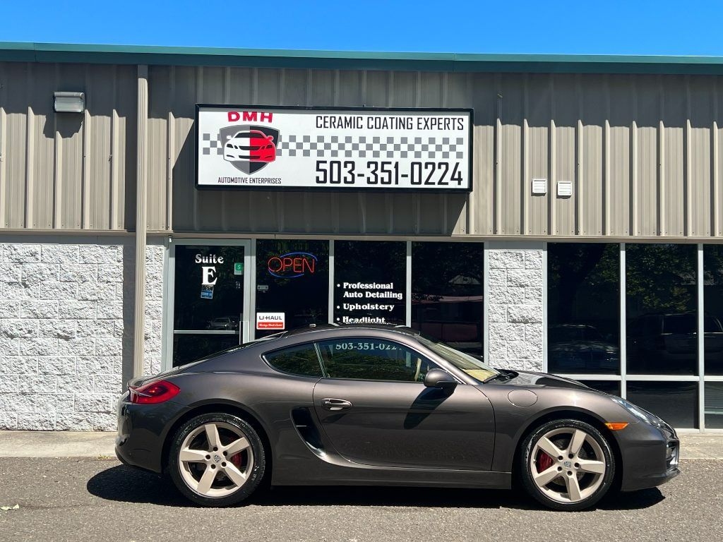 Dark gray sports car parked in front of a business storefront with a DMP sign and phone number.