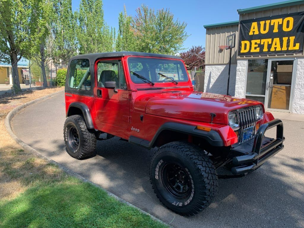 Red Jeep Wrangler parked outside an auto detail shop on a sunny day