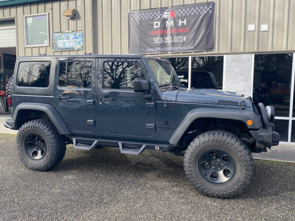 Black Jeep Wrangler parked outside a shop building on a wet lot