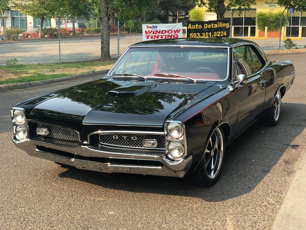 Black classic muscle car parked on a street, viewed from the front-left side