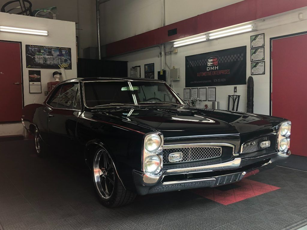 Black classic car in a garage showroom with red and white walls, lit from the front