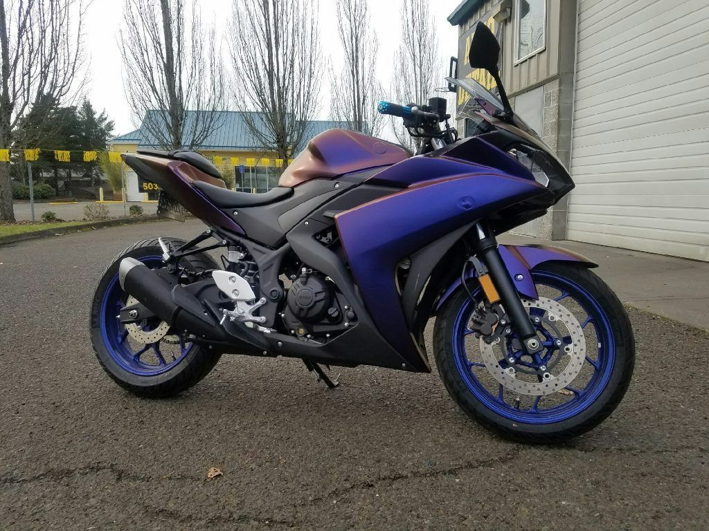 Purple and black sport motorcycle parked on asphalt beside a building