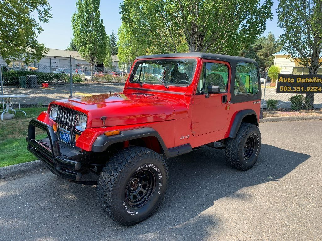 Red Jeep Wrangler parked outdoors on a street, with black fenders and off-road tires.
