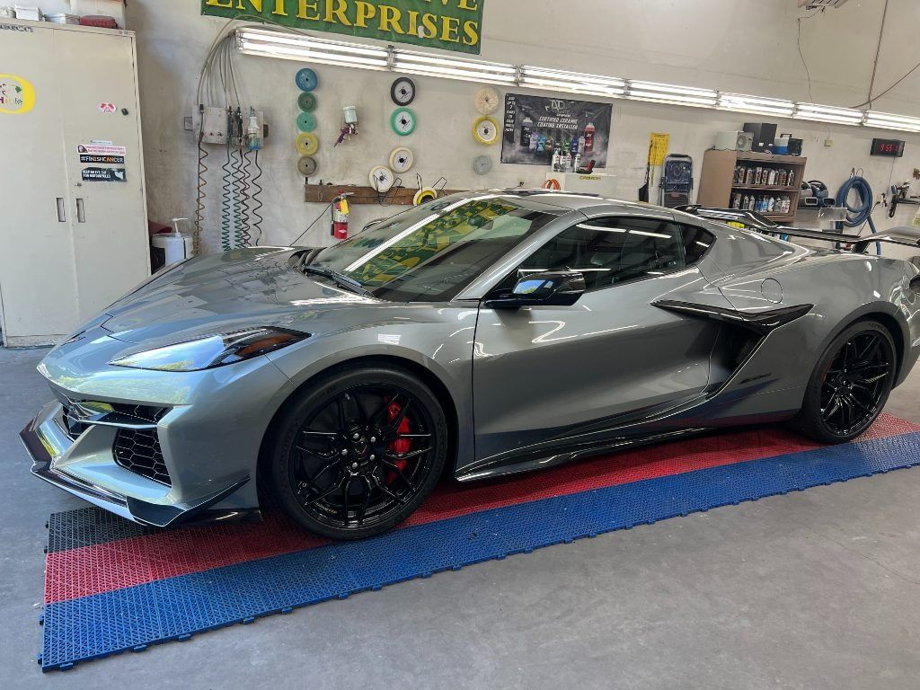 Gray sports car in a garage showroom, parked on a red and blue floor mat.