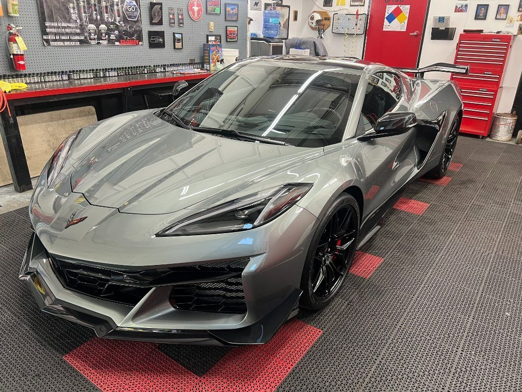 Silver sports car in a garage, surrounded by tools, wall decor, and red tool cabinets.