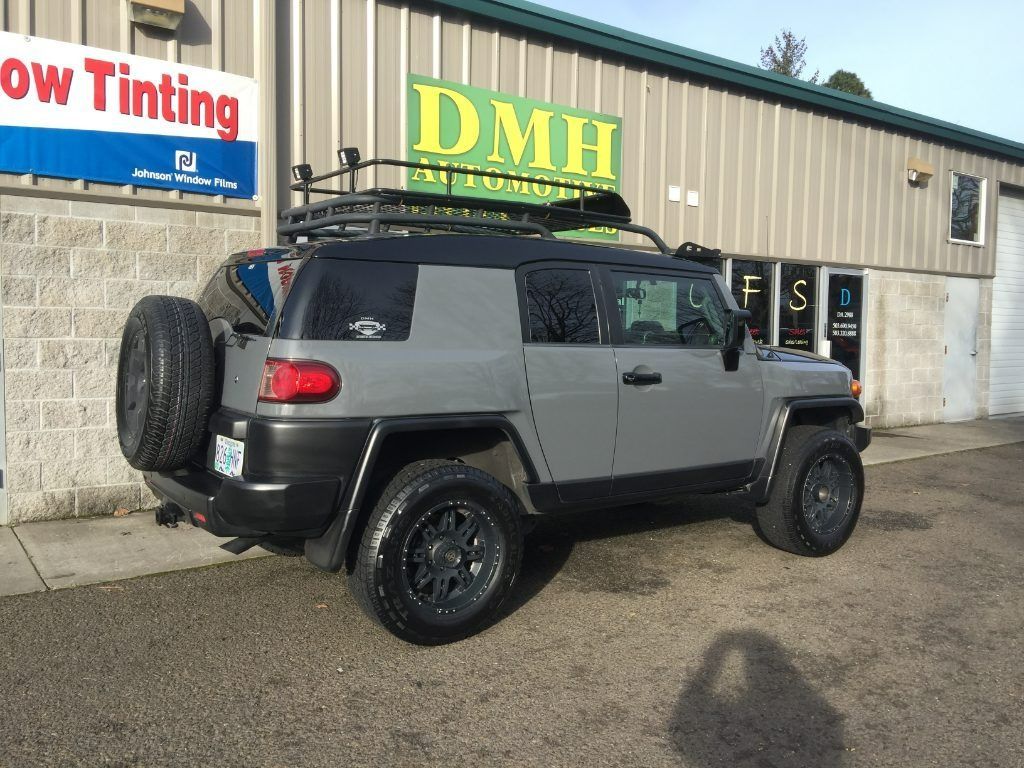 Gray Jeep Wrangler parked outside a building with DMH and window tinting signs