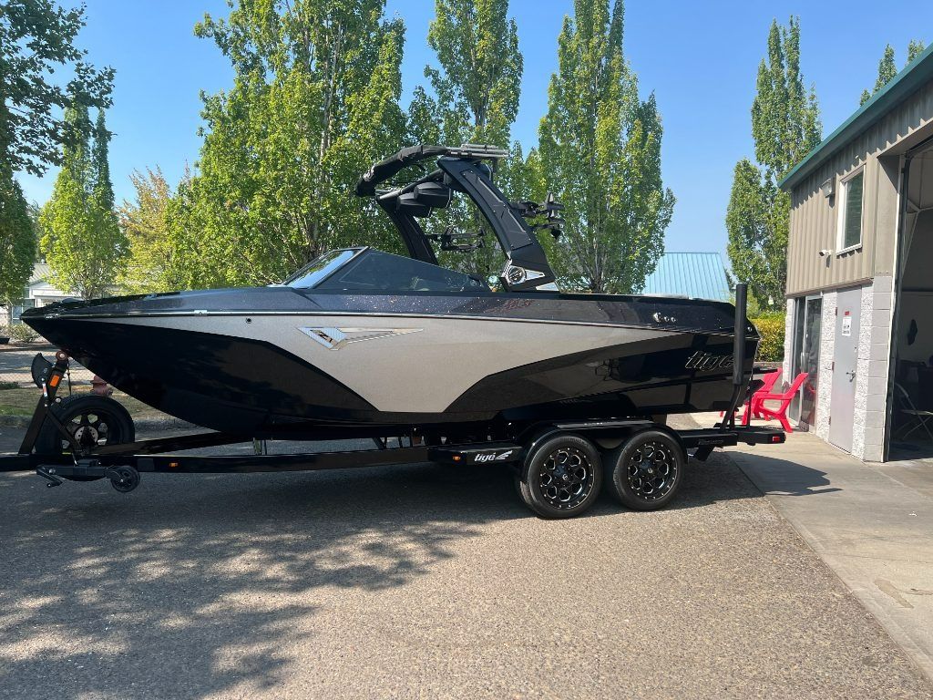 Black-and-tan motorboat on a trailer parked in a driveway beside a house, with trees in the background