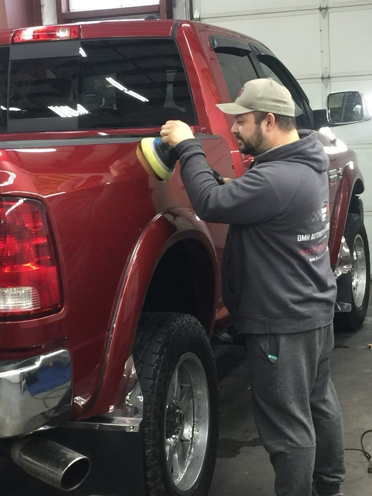 Person polishing a red truck in a garage with a cloth and buffer