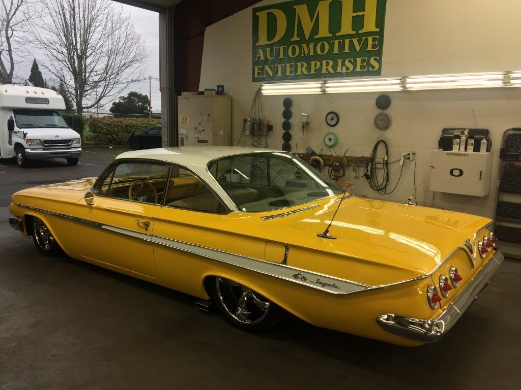 Yellow classic lowrider car parked in a garage with a DMH Automotive Enterprises sign in the background