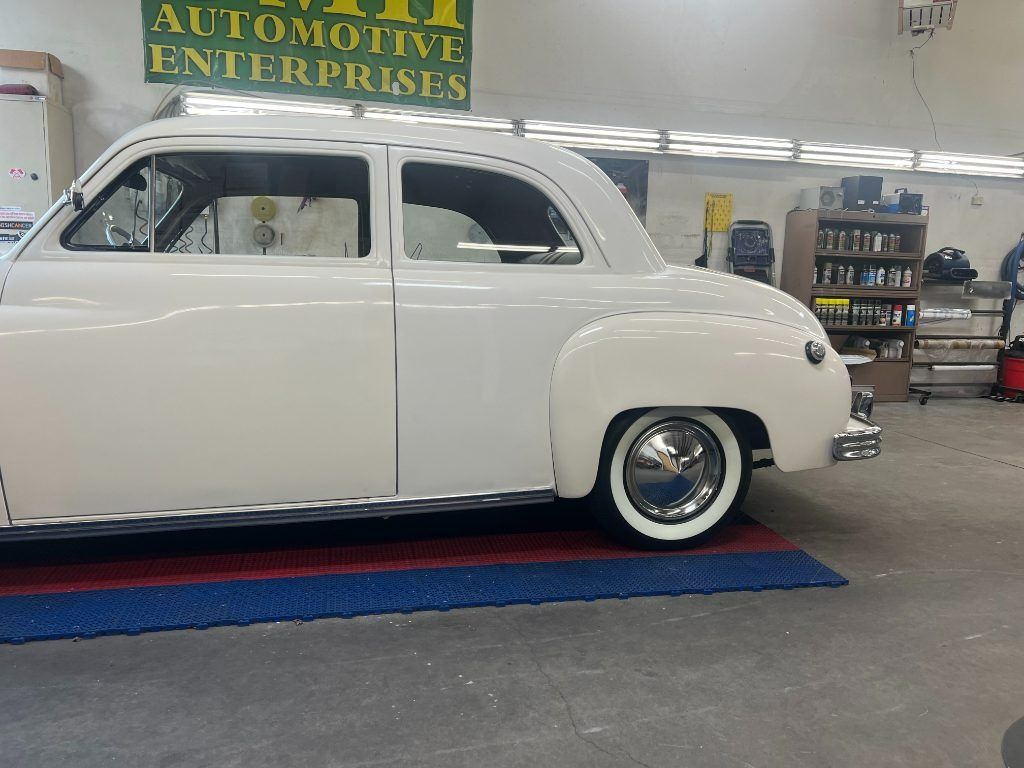 White vintage car in an automotive shop, parked on a blue lift mat with a sign in the background