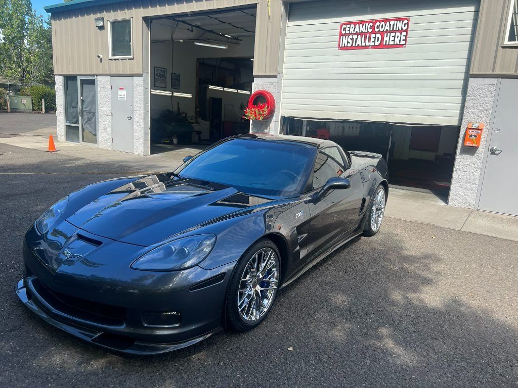 Black sports car parked outside a garage with open bay doors and a “vehicles” sign