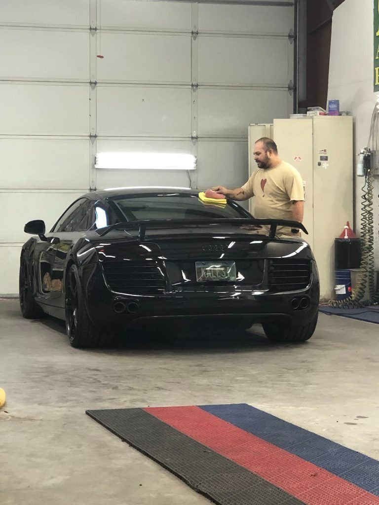 Black sports car being wiped down inside a garage by a person holding a cloth.