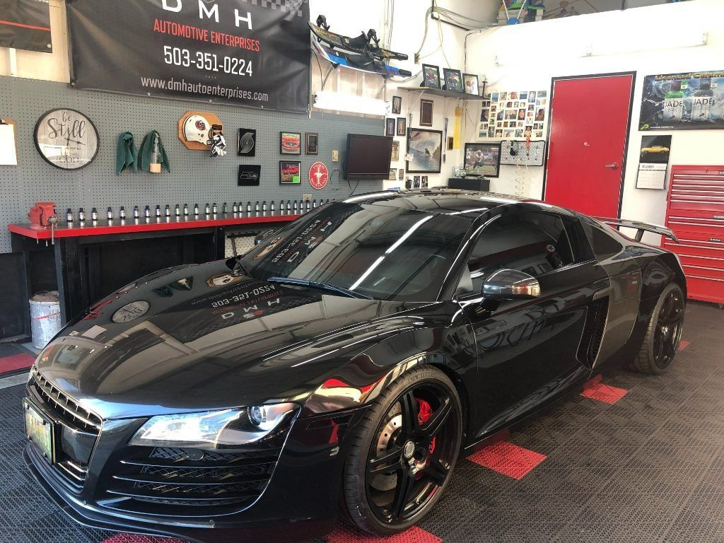 Black sports car in an auto shop garage with a red door and tools on the walls