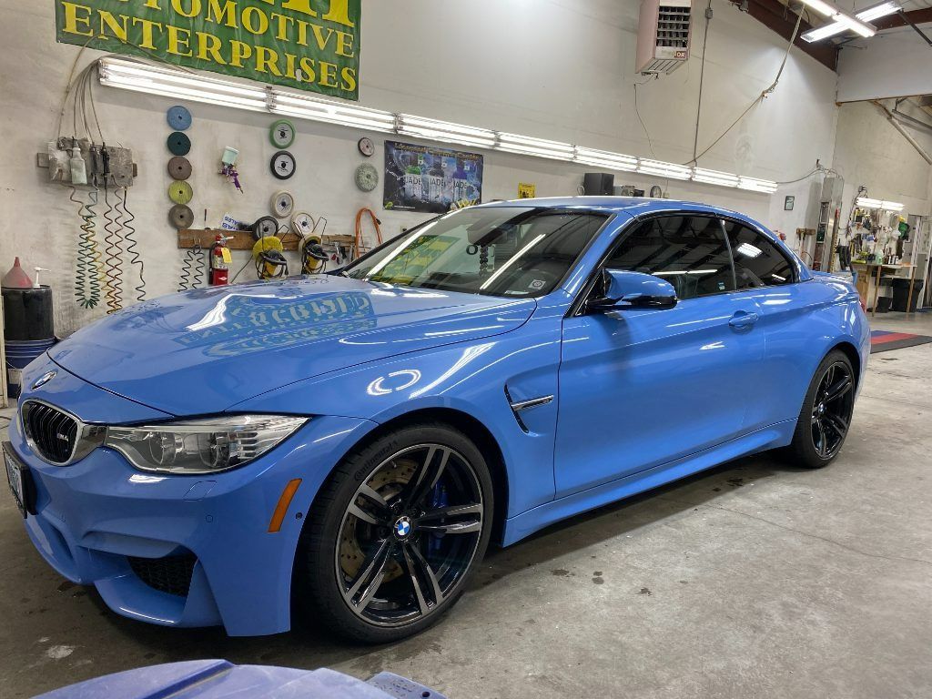 Blue BMW sedan in a garage workshop, angled front view with black rims