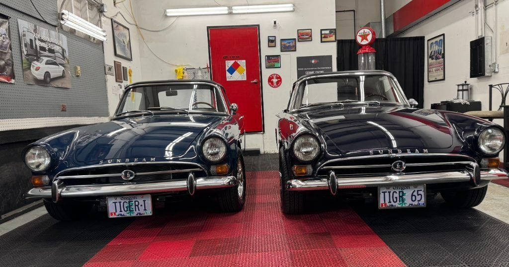 Two classic black cars parked side by side in a garage showroom with red flooring.