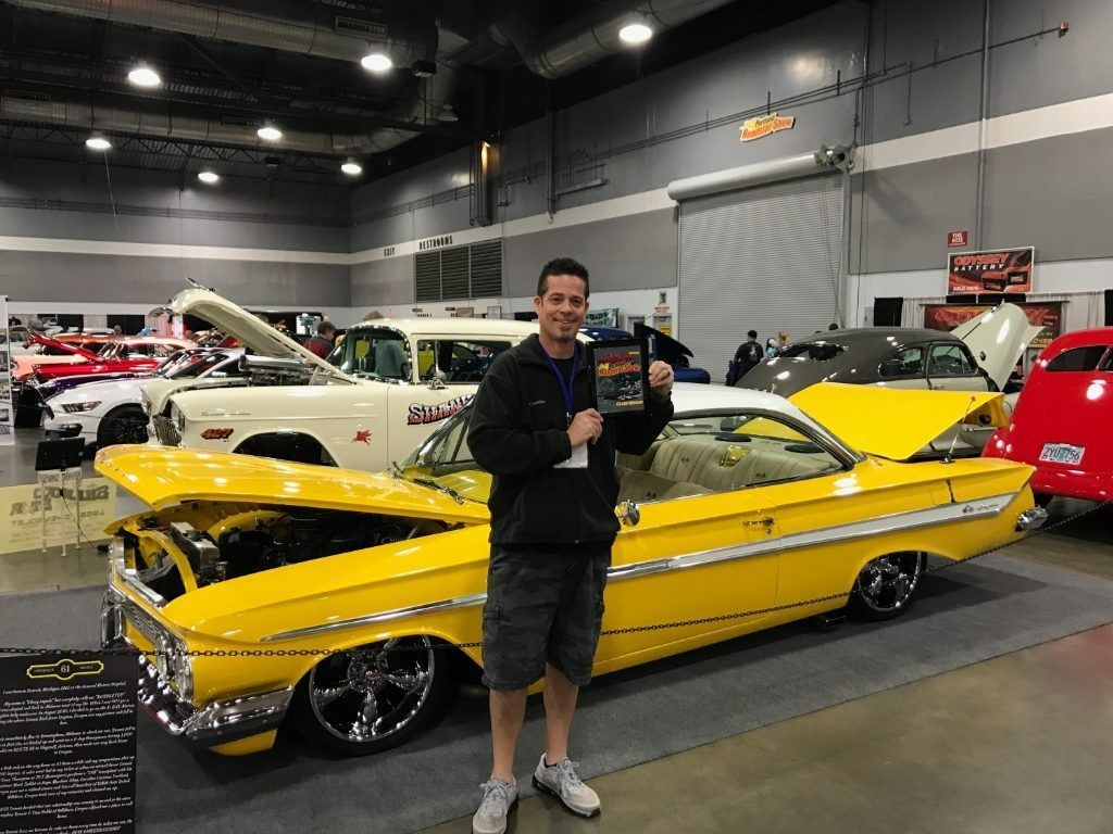 Man posing beside a bright yellow classic car at an indoor car show