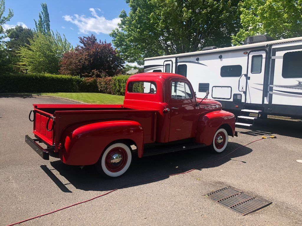 Bright red vintage pickup truck parked beside a white RV in a sunny lot