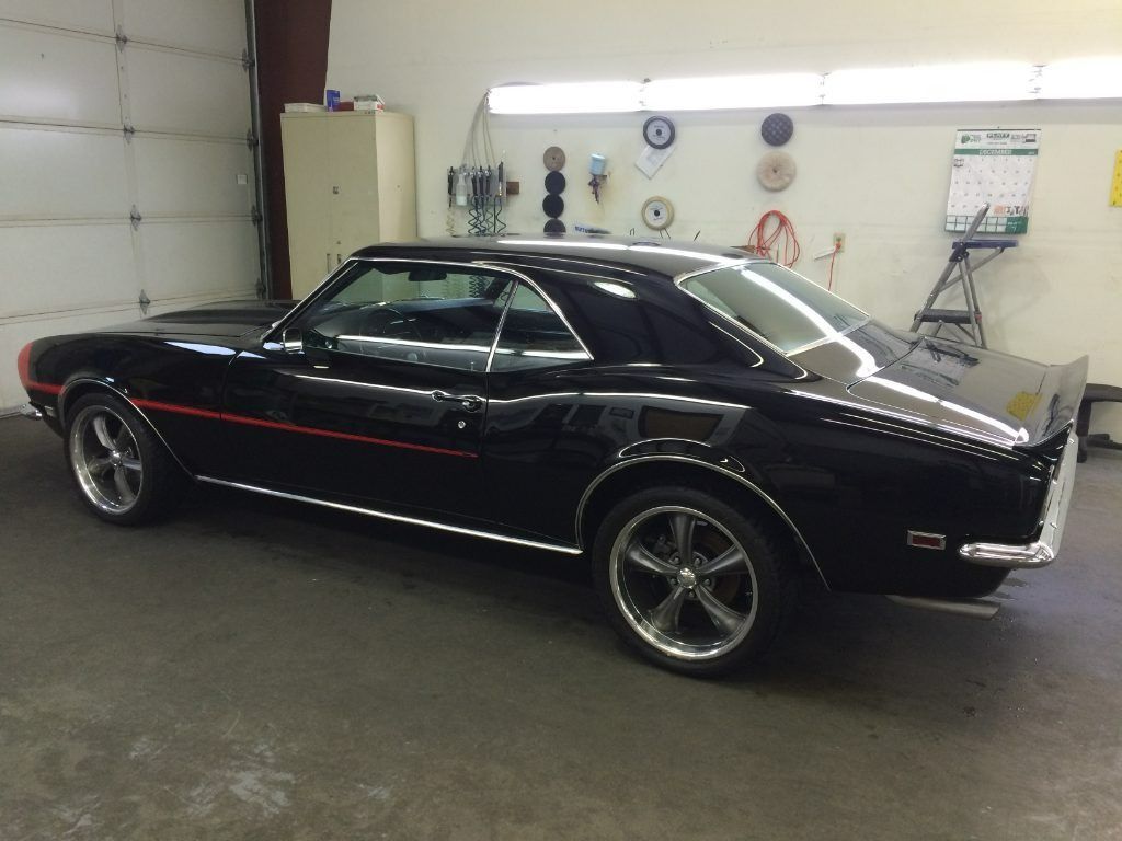 Black classic muscle car with red pinstripe parked inside a garage