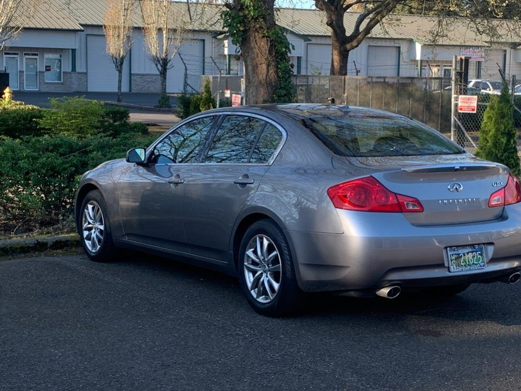 Gray sedan parked on a street beside bushes and buildings, rear view in daylight