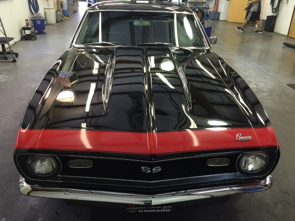 Black classic muscle car with a red hood stripe in an indoor garage