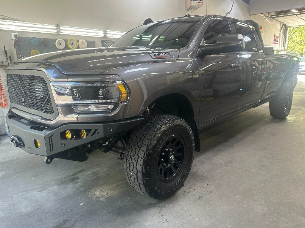 Gray lifted pickup truck parked in a garage, with black off-road tires and a custom front bumper