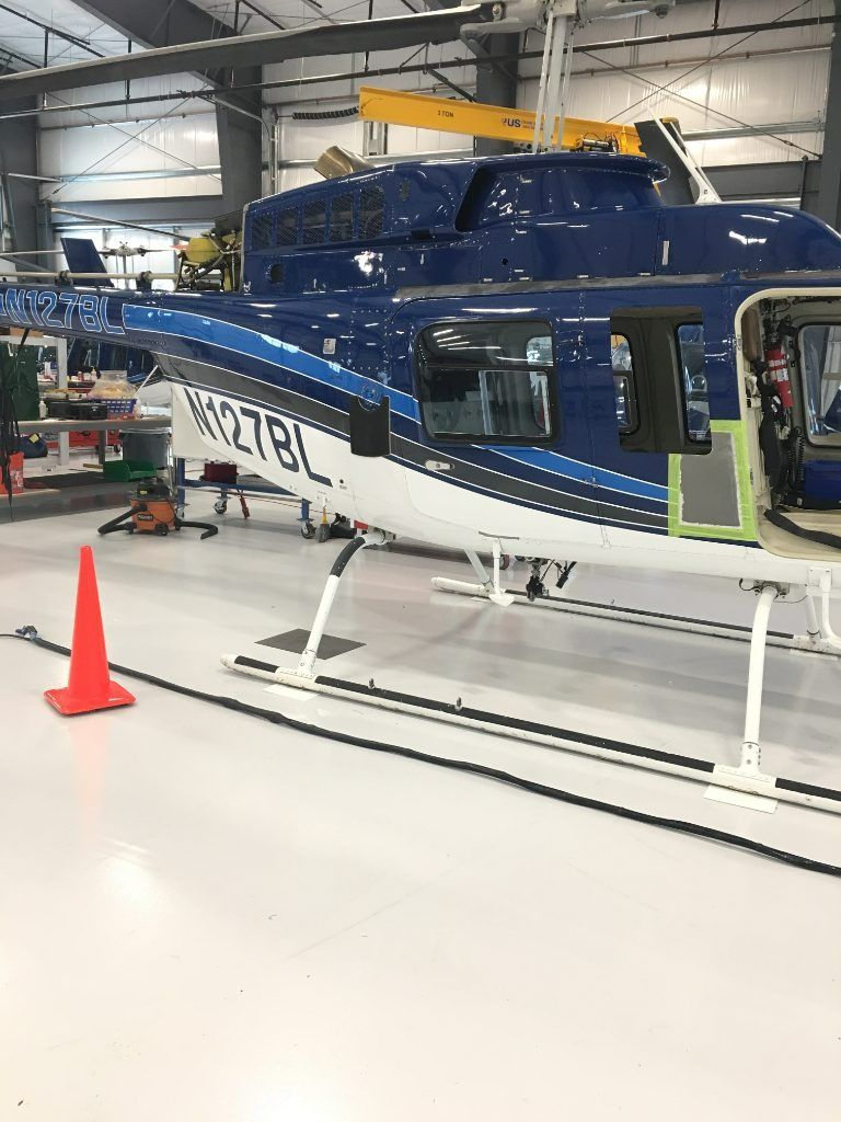 Blue helicopter inside a hangar, with orange cone and white support stands nearby.