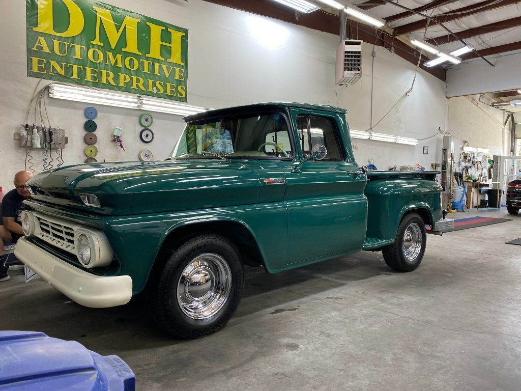 Green vintage pickup truck in an auto shop garage with a DMH Automotive Enterprises sign on the wall