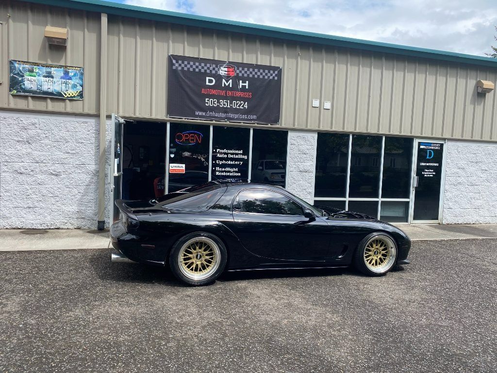 Black sports car parked outside a storefront with a DMW sign, in front of glass windows.
