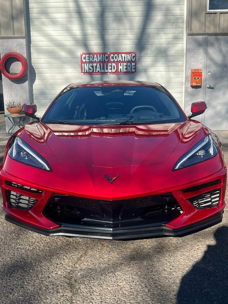 Red Chevrolet Corvette parked in front of a detail shop sign saying “Ceramic Coating Installation Here”