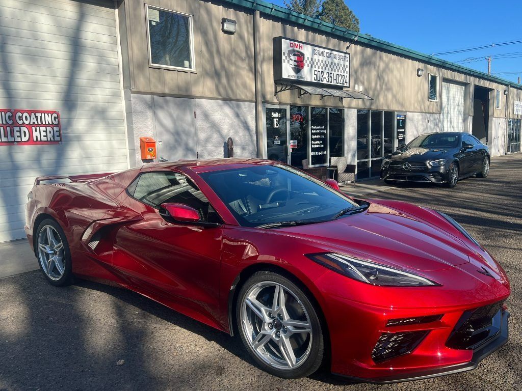 Red sports car parked outside an auto body shop on a sunny street.