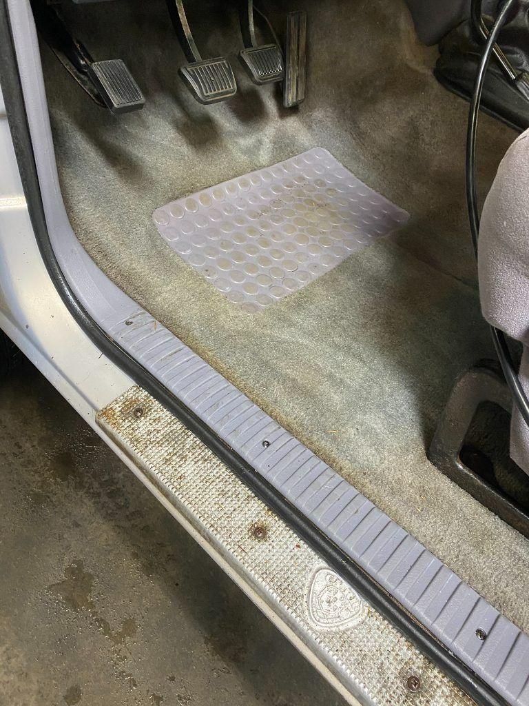 Car footwell with pedals, a textured floor mat, and a silver door sill trim strip