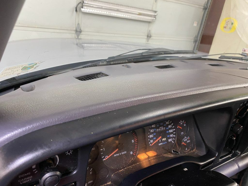 Inside a car, close-up of the dashboard and steering wheel in a garage, with instrument lights on.