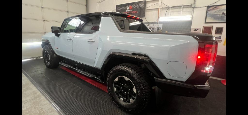 White off-road pickup truck in a workshop, shown from the rear three-quarter view with taillights on.