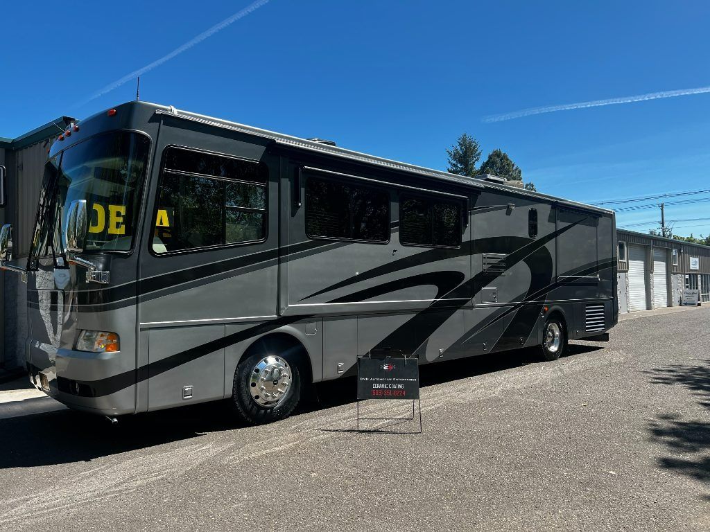 Gray and black motorcoach bus parked on a gravel lot under a clear blue sky