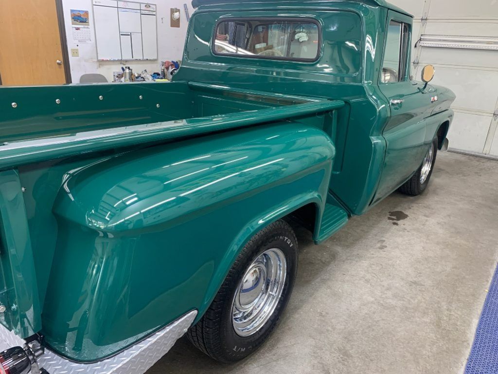 Green vintage pickup truck in a garage, viewed from the rear side.