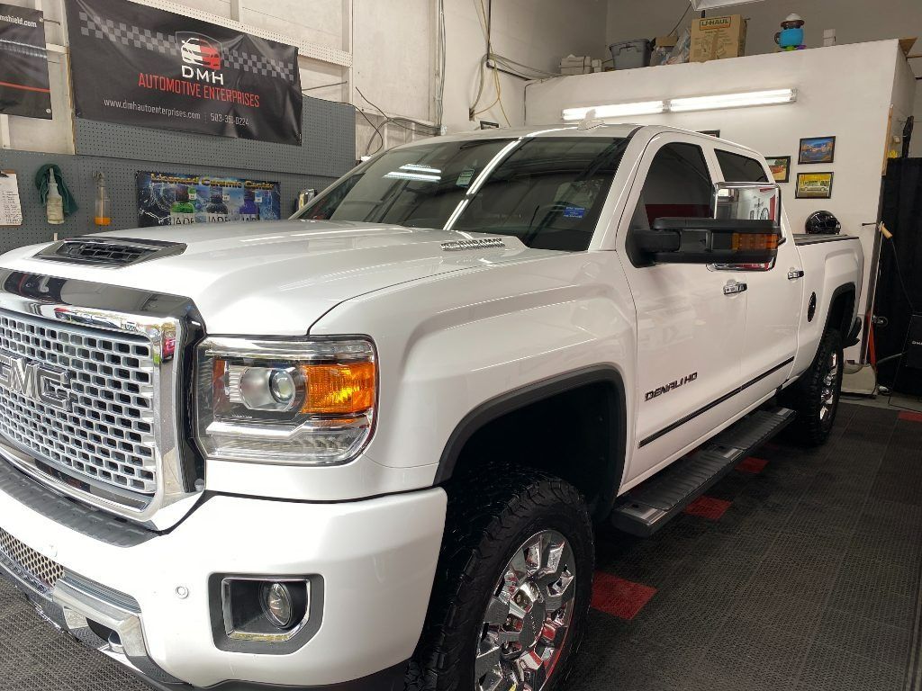 White GMC pickup truck parked indoors in a garage, front-left view with chrome grille and black running boards