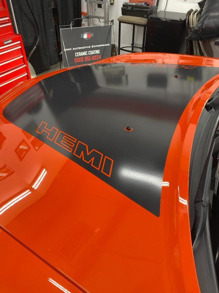 Orange car hood with black center panel and “HEMI” lettering in a garage or workshop
