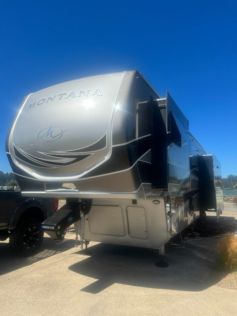 Silver fifth-wheel RV trailer parked in a lot under a bright blue sky