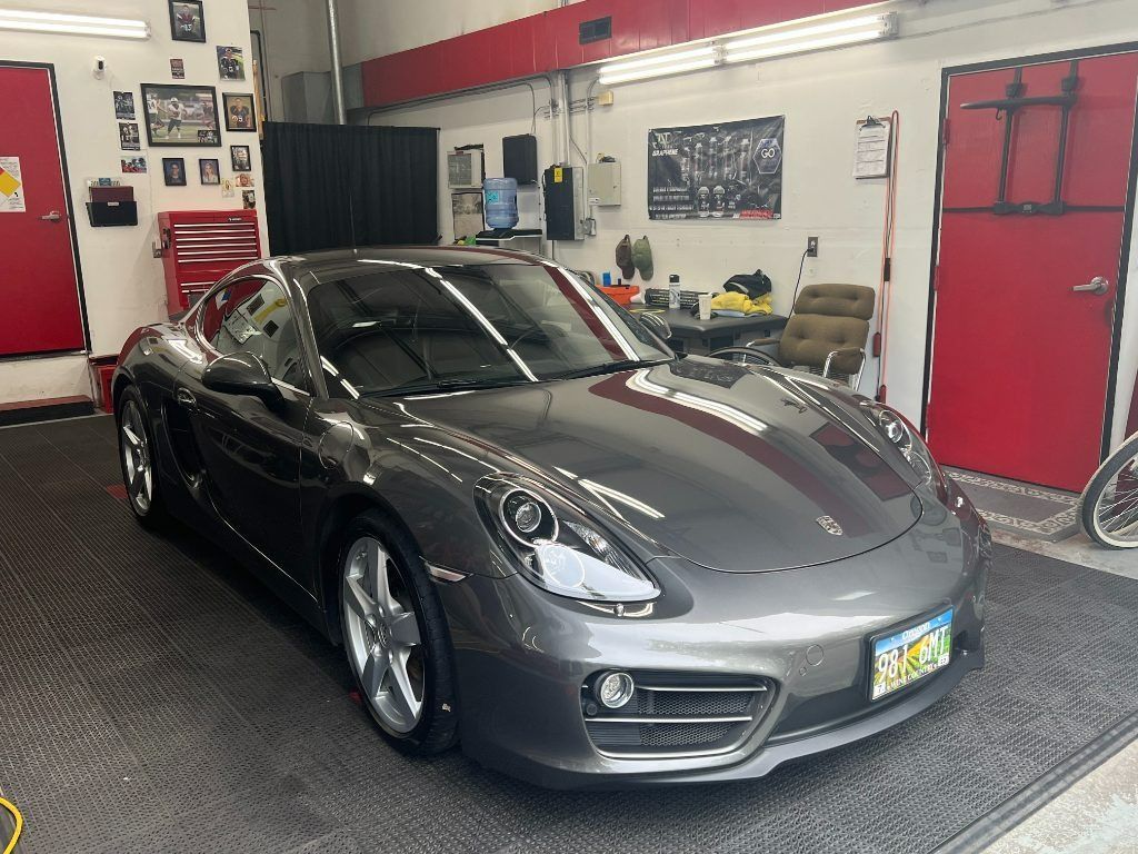 Gray sports car parked in an auto shop garage with red doors and tools in the background