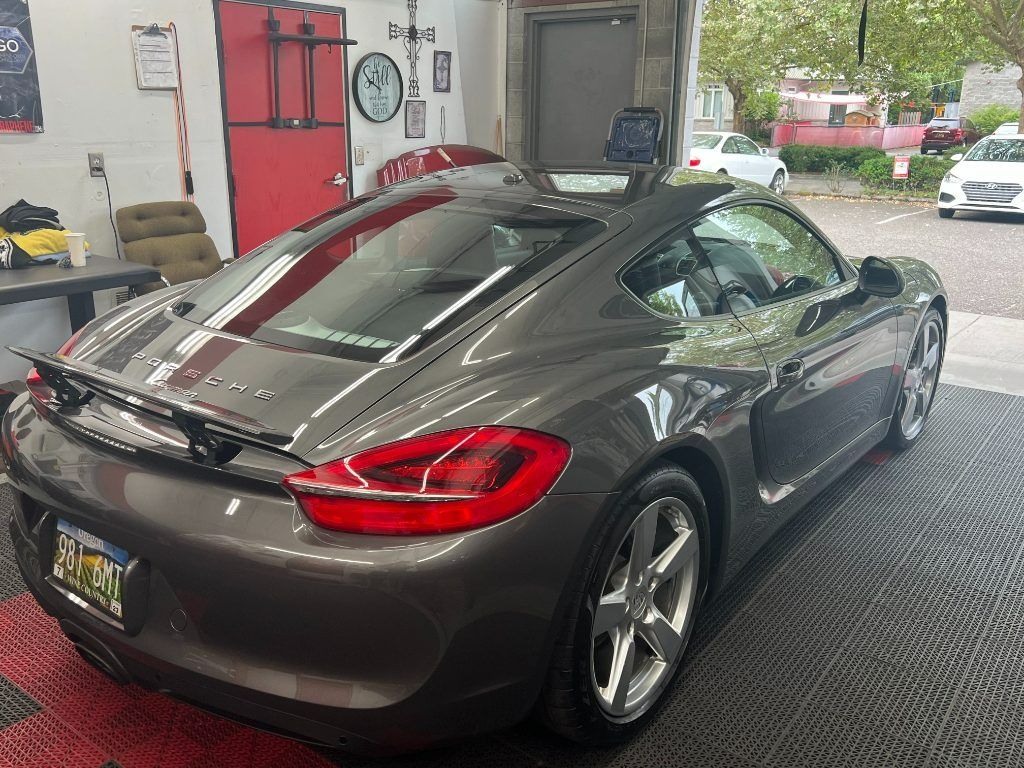 Gray sports coupe in an auto shop, shown from the rear with a red brake light visible.