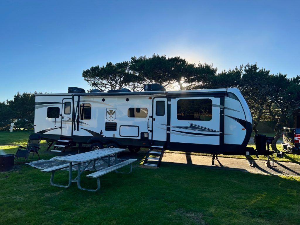 White RV trailer parked on grass with picnic table and awning at sunset