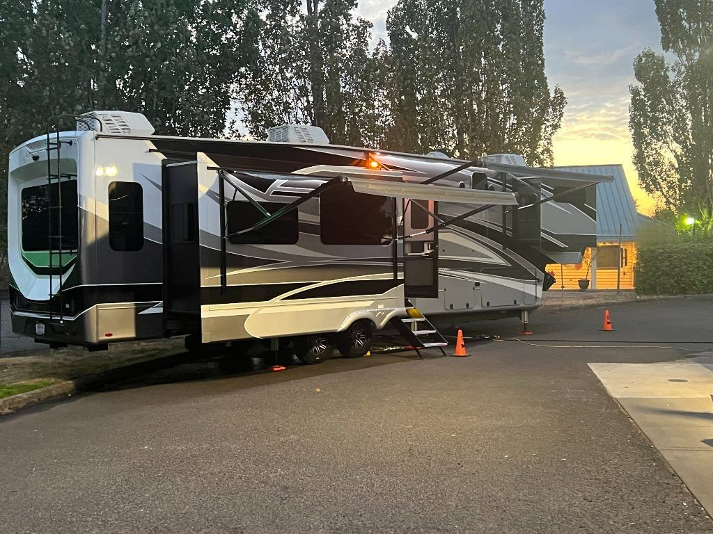 Large black-and-white RV parked at dusk with orange cones beside a tree-lined road